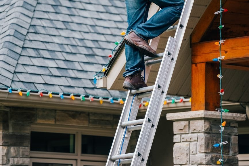 Man on a ladder installing outdoor Christmas lights.